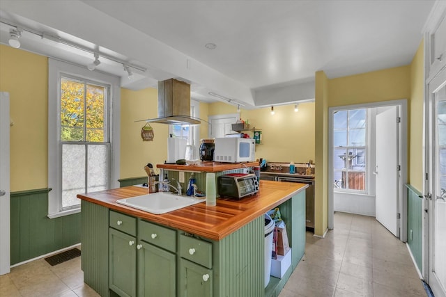 kitchen with sink, green cabinetry, island range hood, butcher block counters, and a center island with sink