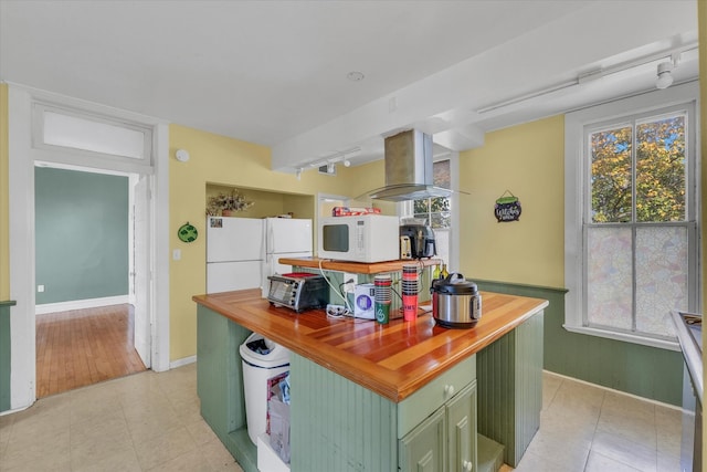 kitchen with white appliances, green cabinetry, butcher block counters, island exhaust hood, and light tile patterned floors