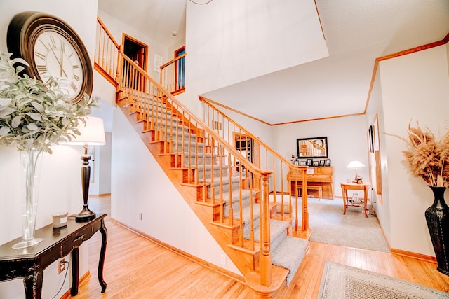 staircase with crown molding, a high ceiling, wood finished floors, and baseboards