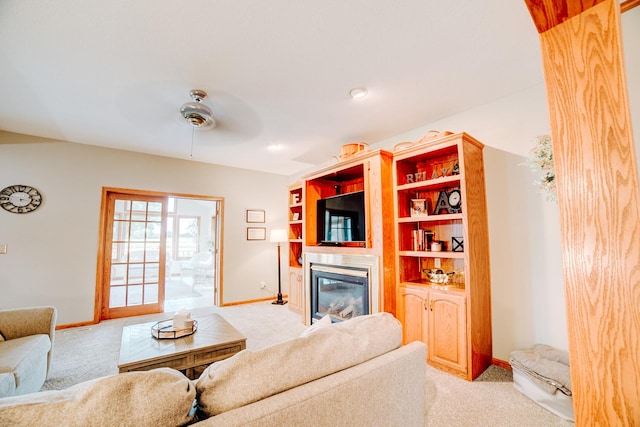 living area featuring ceiling fan, baseboards, light carpet, and a glass covered fireplace