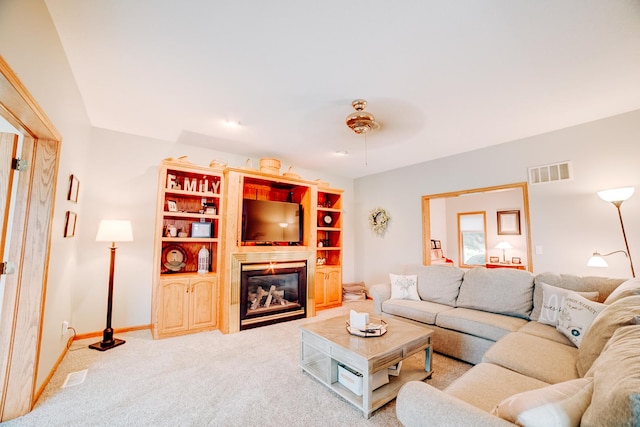 carpeted living room with visible vents, baseboards, a ceiling fan, and a glass covered fireplace
