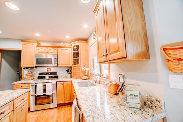 kitchen with light brown cabinetry, light hardwood / wood-style flooring, stainless steel appliances, sink, and light stone counters