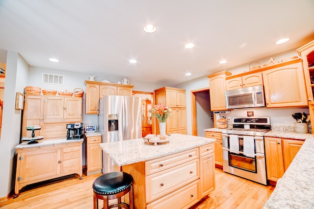 kitchen with light brown cabinets, light hardwood / wood-style flooring, stainless steel appliances, and a kitchen bar