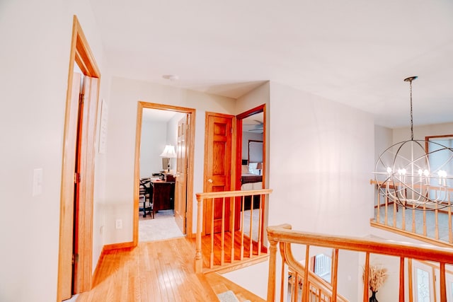 corridor with a notable chandelier, baseboards, light wood-style floors, and stairway