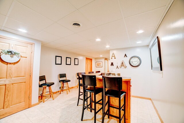 dining room featuring a drop ceiling, bar area, and light tile patterned floors