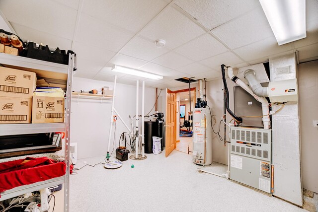 finished below grade area featuring heating unit, a paneled ceiling, and water heater