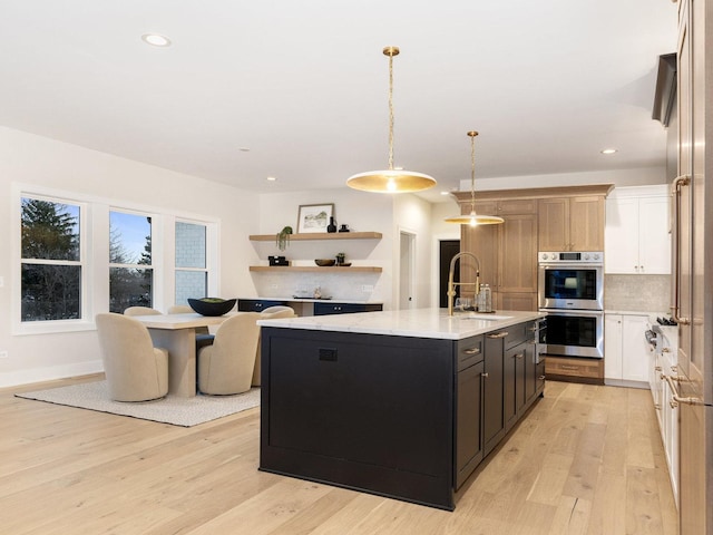 kitchen with stainless steel double oven, backsplash, decorative light fixtures, a kitchen island with sink, and sink