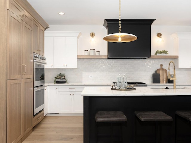 kitchen with backsplash, light hardwood / wood-style flooring, hanging light fixtures, white cabinets, and light stone counters