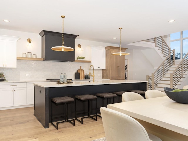 kitchen featuring light hardwood / wood-style floors, hanging light fixtures, a center island with sink, and a kitchen bar