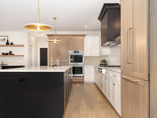 kitchen with white cabinets, stainless steel appliances, an island with sink, sink, and hanging light fixtures