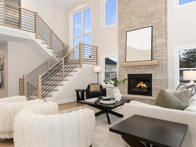 living room featuring a towering ceiling, a wealth of natural light, a stone fireplace, and hardwood / wood-style floors