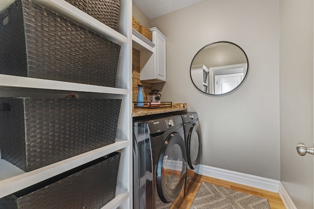 laundry area with light wood-type flooring, washing machine and dryer, and cabinets