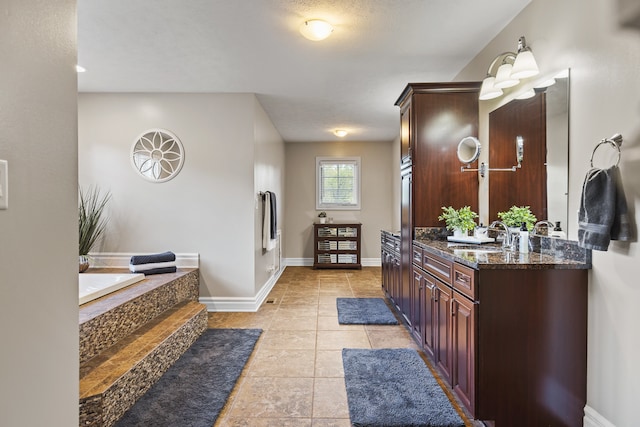 bathroom with a textured ceiling, tile patterned flooring, vanity, and a tub to relax in