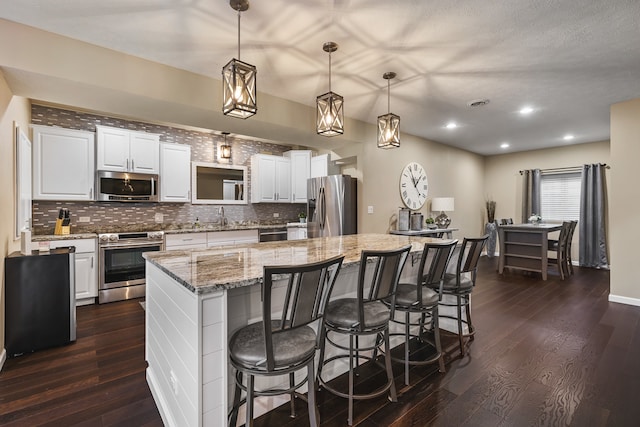 kitchen featuring stainless steel appliances, dark hardwood / wood-style floors, decorative light fixtures, a spacious island, and white cabinets