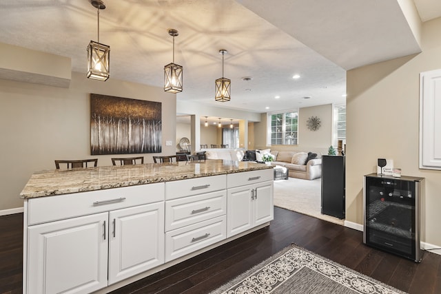 kitchen featuring white cabinetry, wine cooler, a kitchen bar, hanging light fixtures, and dark wood-type flooring