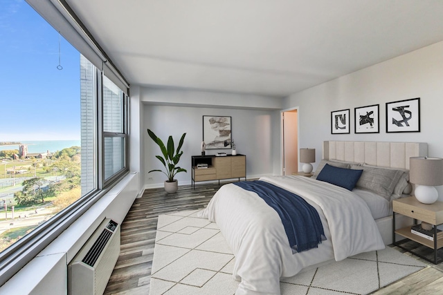 bedroom featuring hardwood / wood-style floors, an AC wall unit, and a water view