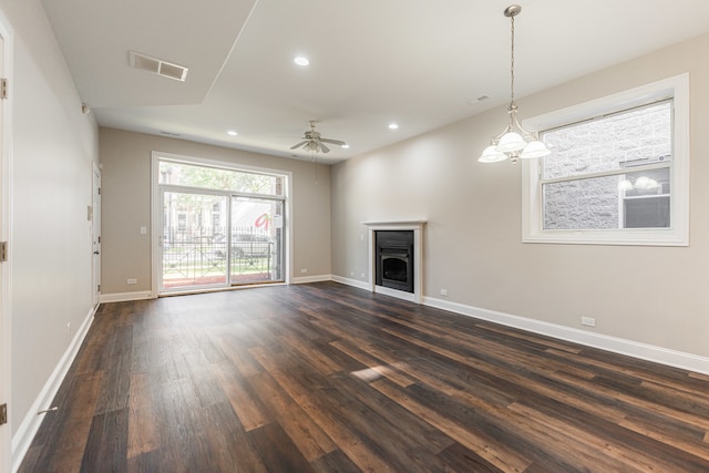 unfurnished living room with ceiling fan with notable chandelier and dark wood-type flooring