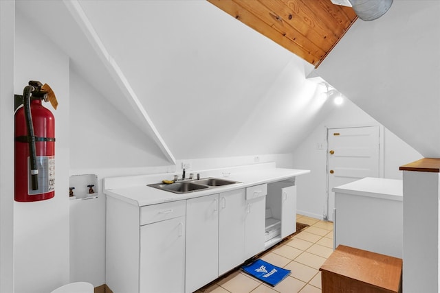 interior space with white cabinetry, sink, light tile patterned floors, and vaulted ceiling