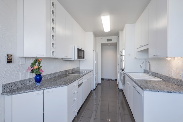 kitchen with white cabinetry, white appliances, dark tile patterned floors, dark stone counters, and sink