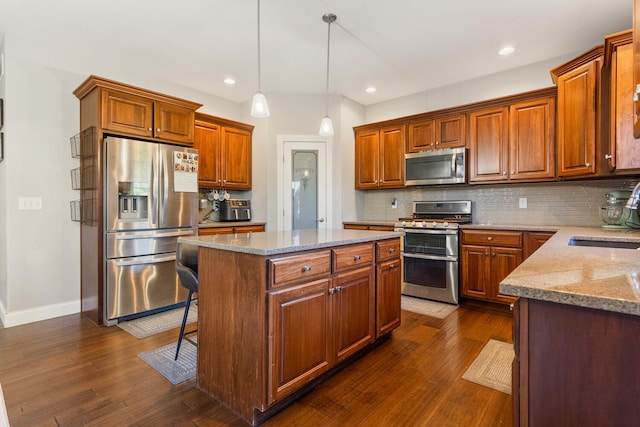 kitchen with sink, a kitchen island, decorative light fixtures, appliances with stainless steel finishes, and dark hardwood / wood-style floors