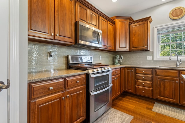 kitchen featuring sink, tasteful backsplash, stainless steel appliances, light stone countertops, and dark hardwood / wood-style flooring