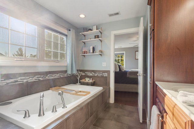 bathroom featuring tiled tub, vanity, and tile patterned flooring