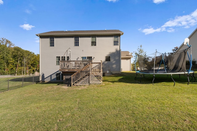 rear view of property featuring a wooden deck, a trampoline, and a lawn