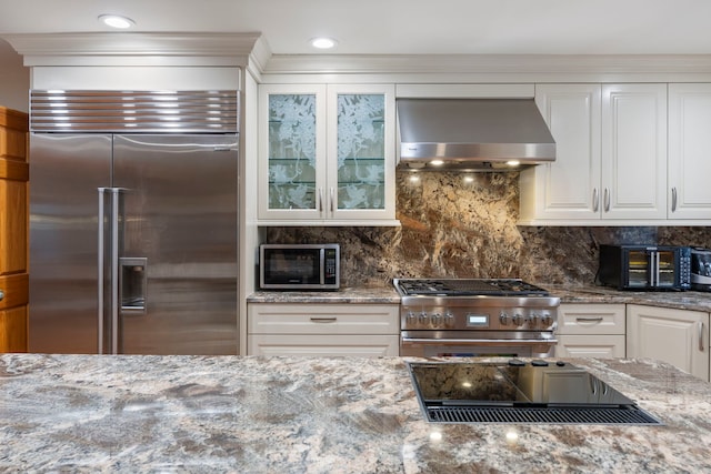 kitchen with black appliances, white cabinets, wall chimney range hood, and light stone counters