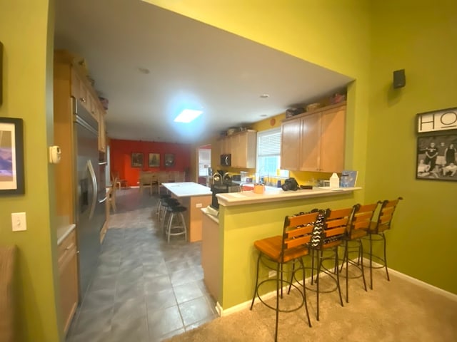 kitchen featuring kitchen peninsula, a kitchen breakfast bar, stainless steel appliances, light tile patterned floors, and light brown cabinetry