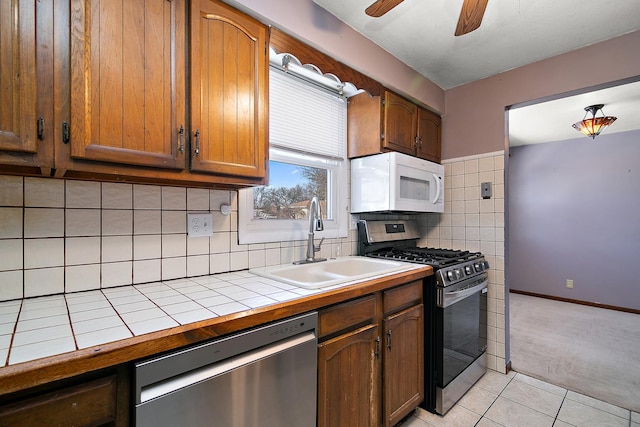 kitchen featuring appliances with stainless steel finishes, sink, light tile patterned floors, tile countertops, and decorative backsplash