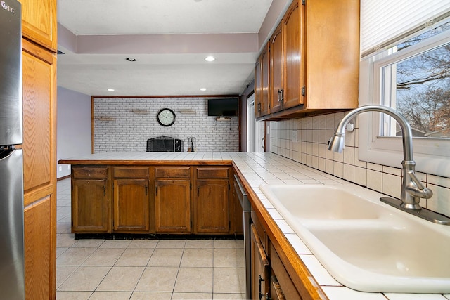 kitchen with tile counters, decorative backsplash, sink, kitchen peninsula, and light tile patterned flooring