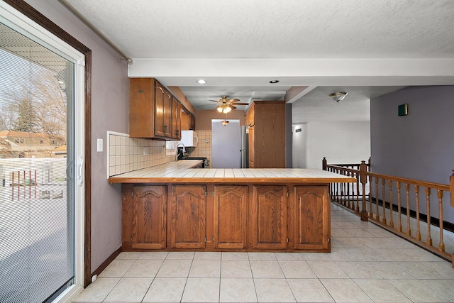 kitchen featuring kitchen peninsula, ceiling fan, sink, tasteful backsplash, and tile counters