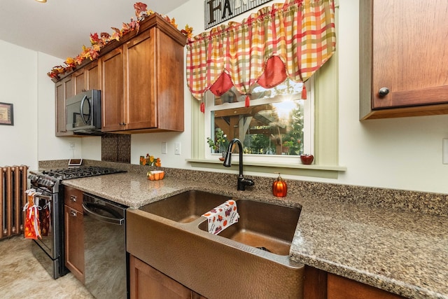 kitchen with appliances with stainless steel finishes, sink, radiator, and dark stone counters