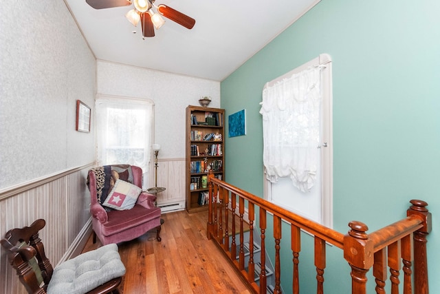 living area featuring ceiling fan, a baseboard radiator, light wood-type flooring, and wooden walls