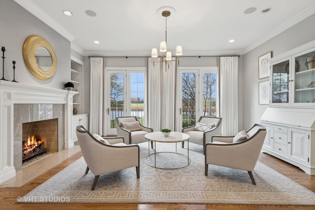 living area featuring built in shelves, a premium fireplace, light hardwood / wood-style flooring, and crown molding