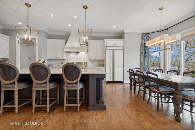 kitchen with custom range hood, white cabinetry, light hardwood / wood-style flooring, and decorative light fixtures