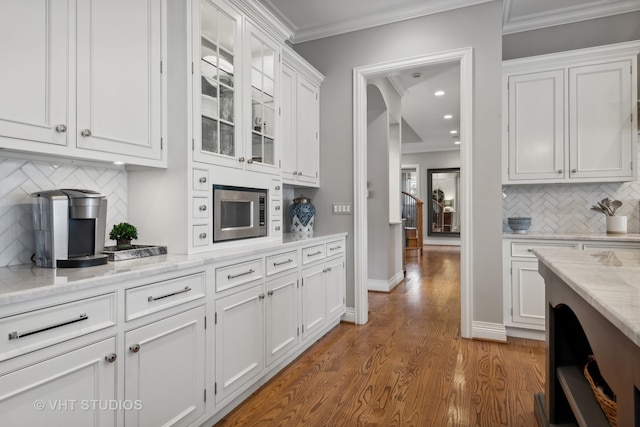 bar featuring hardwood / wood-style flooring, white cabinetry, stainless steel microwave, and ornamental molding