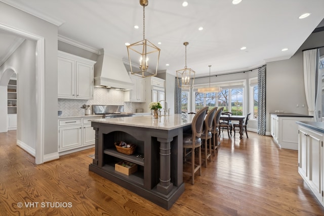 kitchen featuring hanging light fixtures, white cabinets, light hardwood / wood-style flooring, and a kitchen island with sink