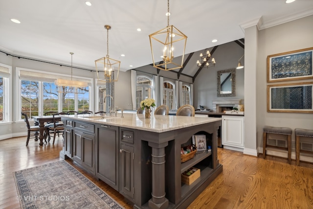 kitchen with sink, light stone counters, light hardwood / wood-style flooring, pendant lighting, and a kitchen island with sink