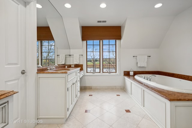 bathroom featuring tile patterned flooring, vanity, lofted ceiling, and a tub to relax in