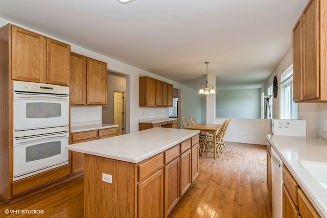 kitchen with light wood-type flooring, a center island, a notable chandelier, hanging light fixtures, and white appliances