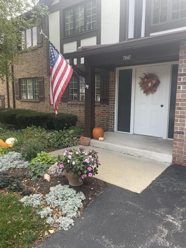 doorway to property with a porch, brick siding, and stucco siding