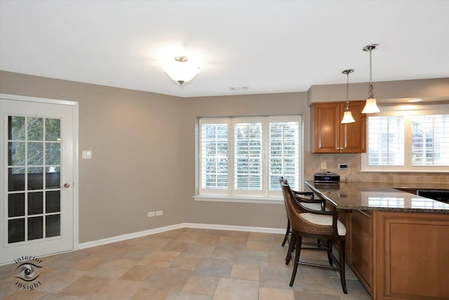 kitchen featuring a breakfast bar, brown cabinets, decorative light fixtures, decorative backsplash, and baseboards