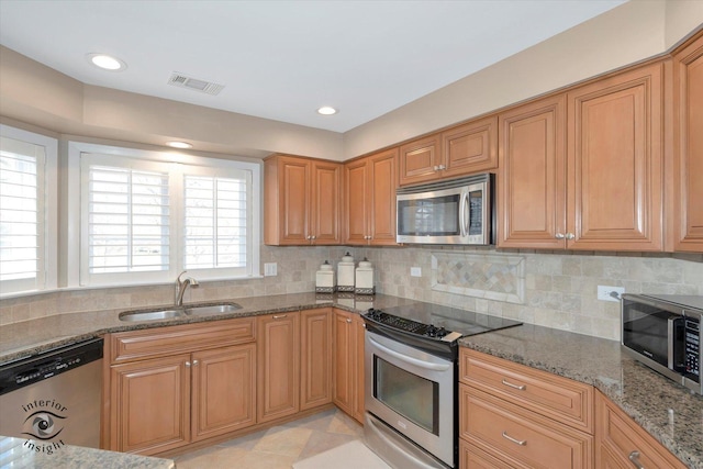 kitchen with visible vents, backsplash, appliances with stainless steel finishes, a sink, and dark stone counters