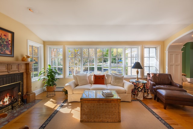 living room with a brick fireplace, light hardwood / wood-style floors, vaulted ceiling, and a baseboard radiator