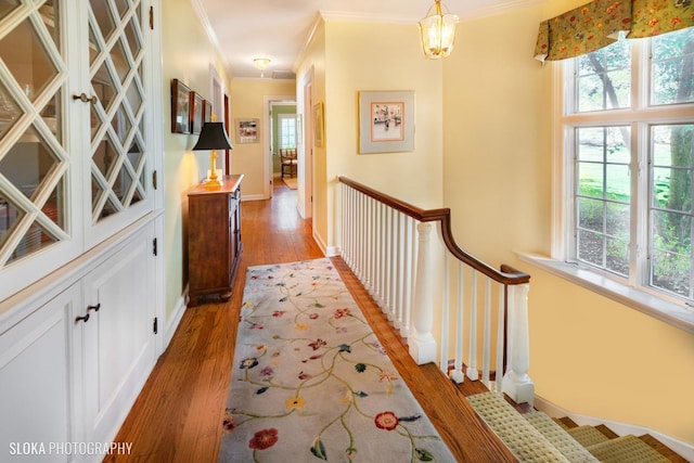 corridor featuring crown molding, light wood-type flooring, baseboards, a notable chandelier, and stairs