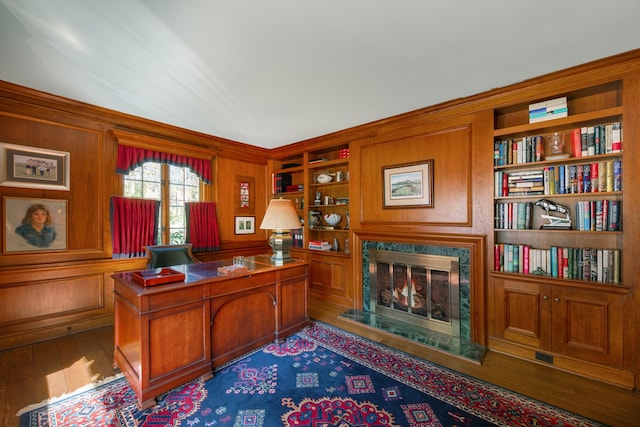 home office featuring built in shelves, a premium fireplace, wooden walls, and wood-type flooring