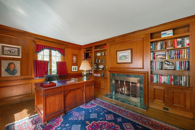 office area featuring wood-type flooring, a premium fireplace, wood walls, and built in features