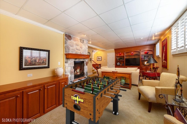 rec room with a drop ceiling, light carpet, ornamental molding, and a fireplace