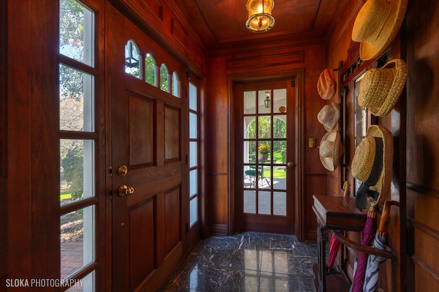 entrance foyer with wood ceiling, crown molding, and wood walls